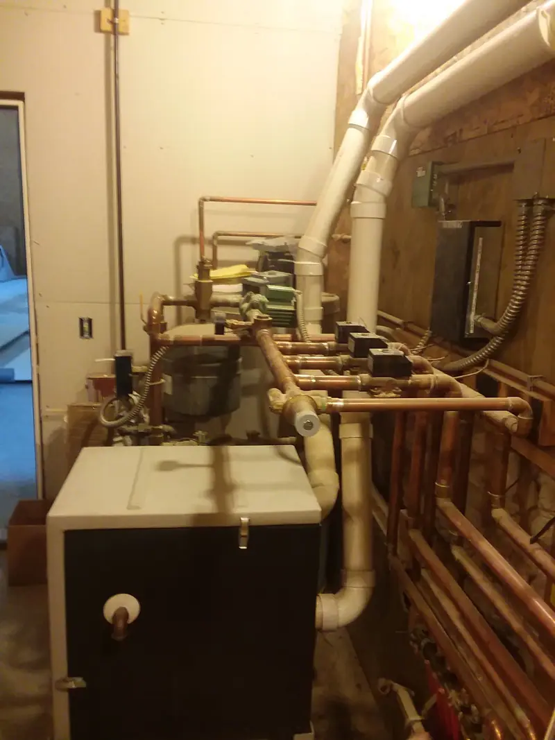 A boiler with copper supply and return manifolds, zone valves and venting in a basement mechanical room
