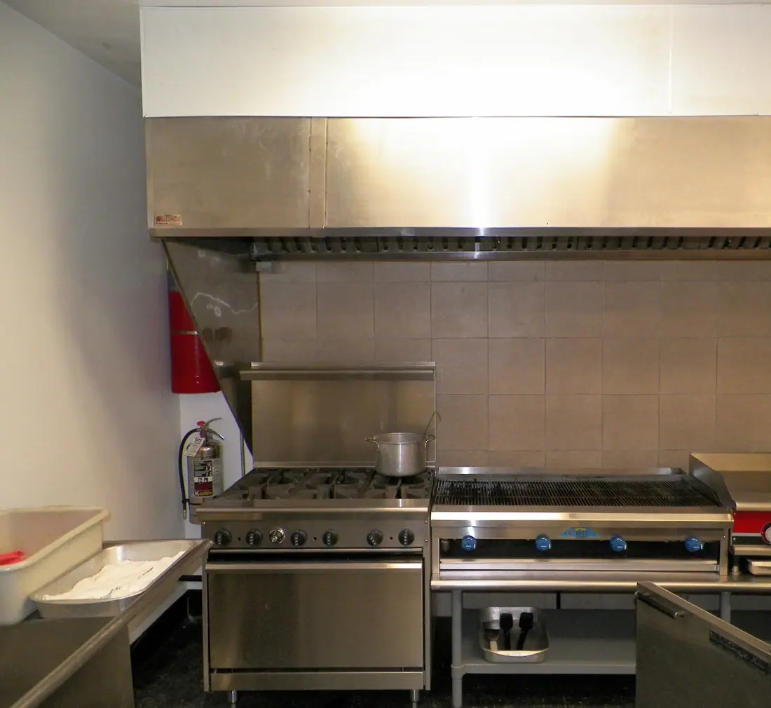 A stainless commercial kitchen hood over a range, charbroiler and griddle line