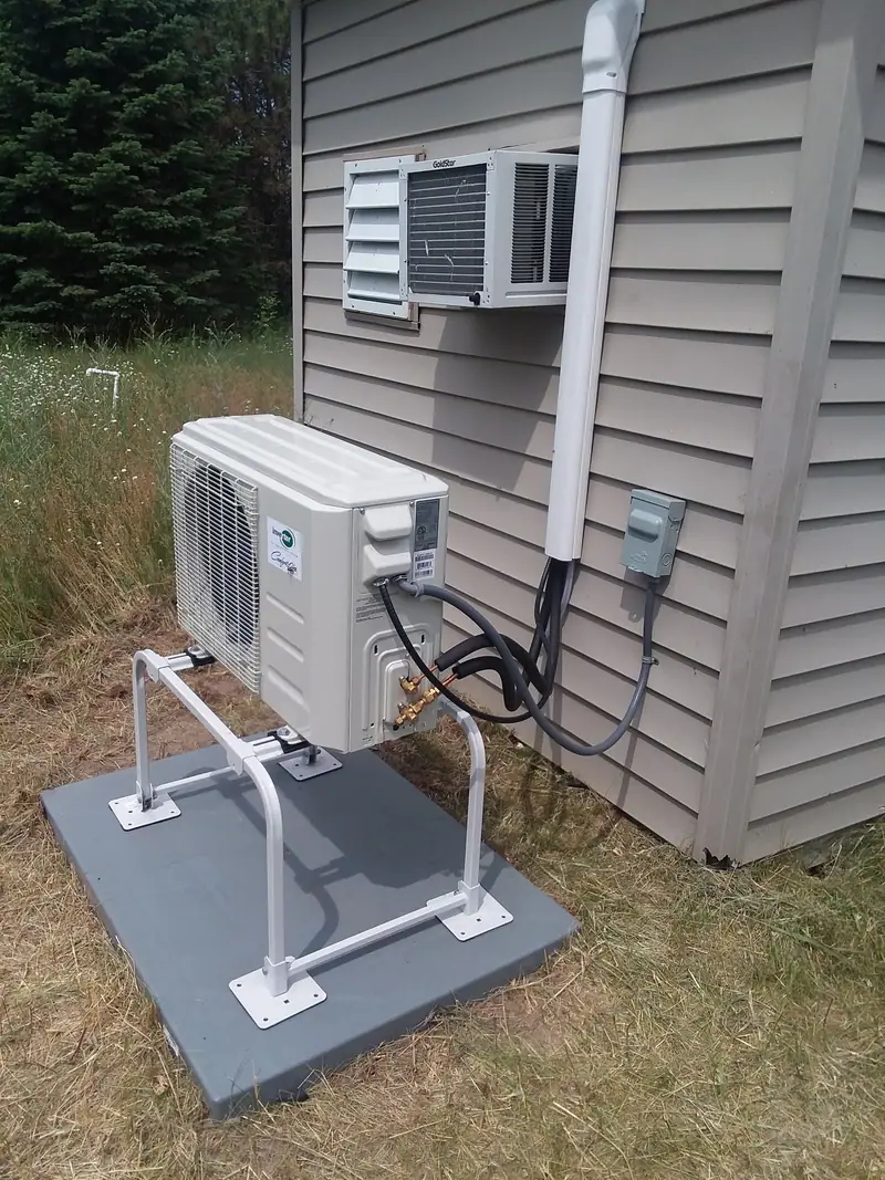 A ductless heat pump outdoor unit on a raised stand and pad, with a covered line set running up the siding