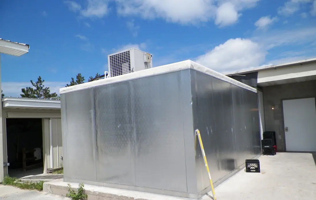 A walk-in cooler box behind a business with its refrigeration condensing unit mounted on the roof